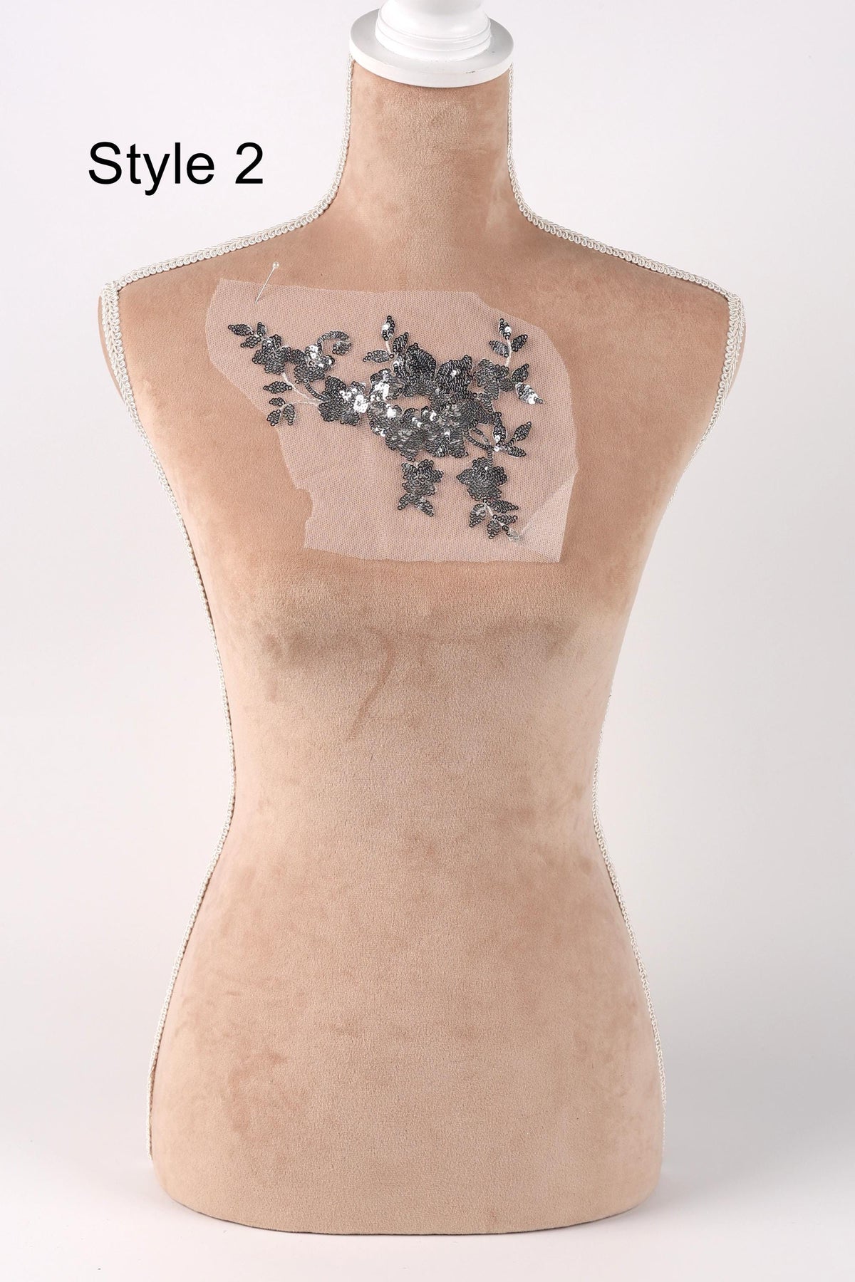 A mannequin with a beige fabric body and a decorative floral embellishment on its chest.