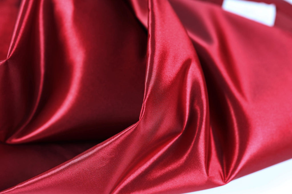 The image is a close-up of a shiny, red satin fabric.