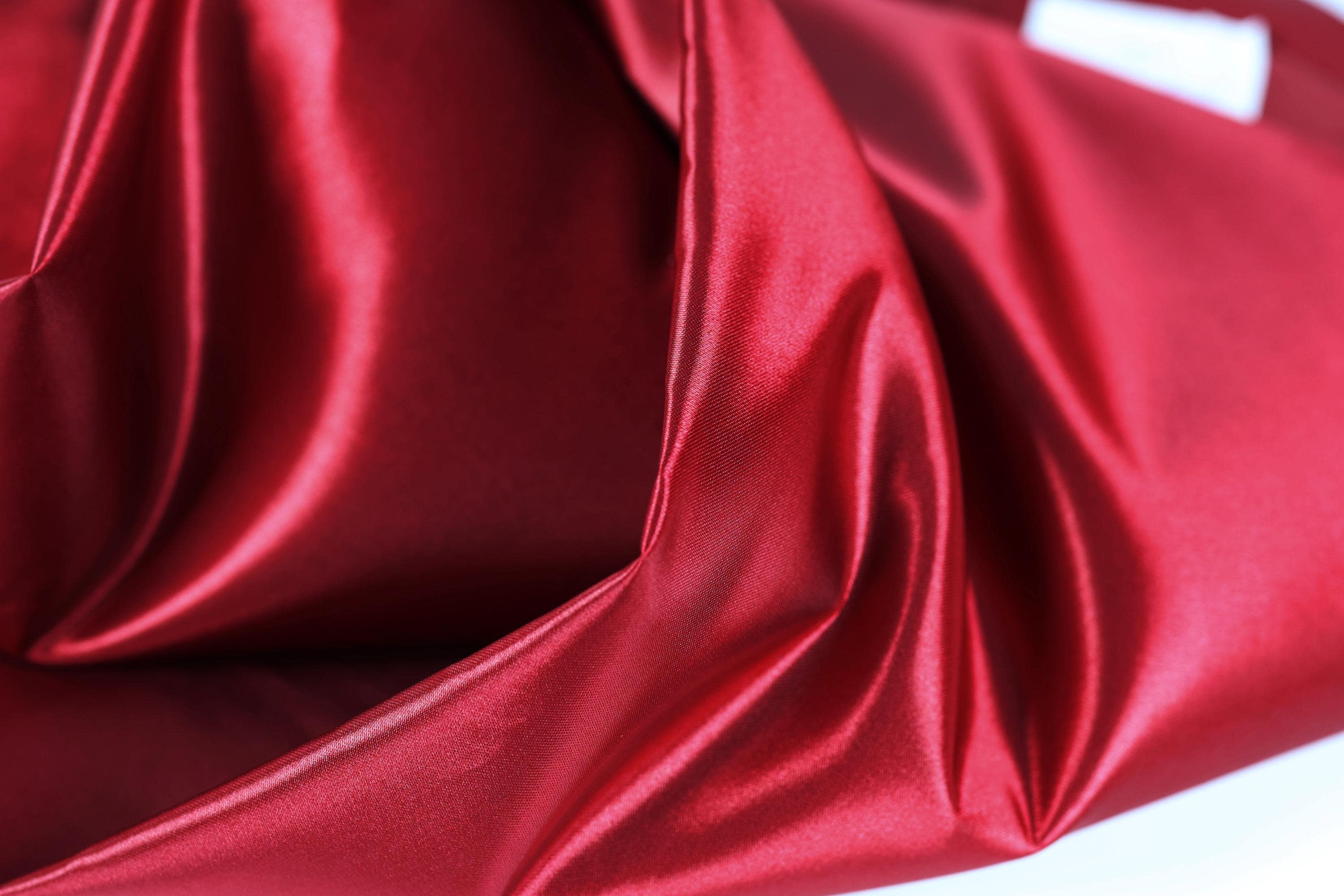 The image is a close-up of a shiny, red satin fabric.