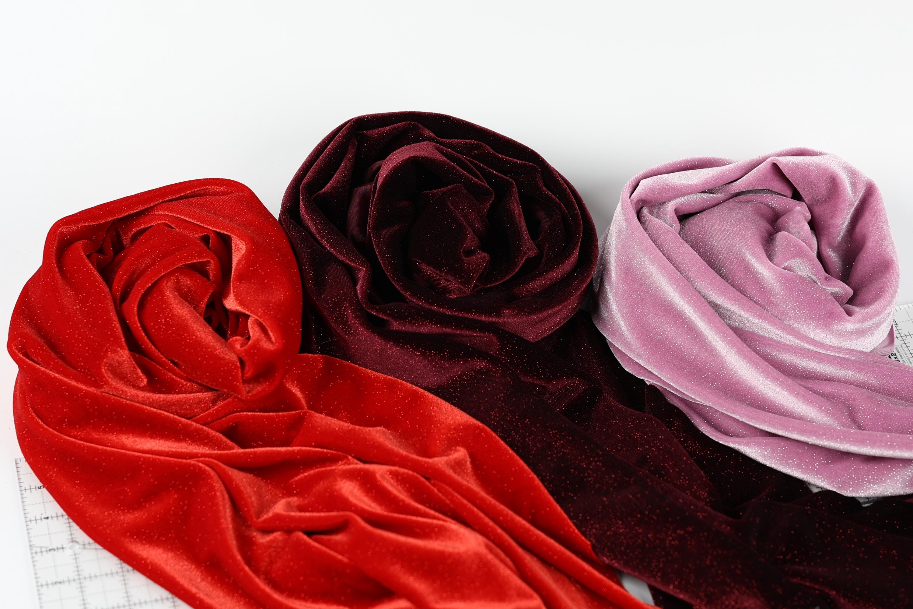 three different colored velvet fabric swatches, including red, burgundy, and pink velvet, arranged on a white background.