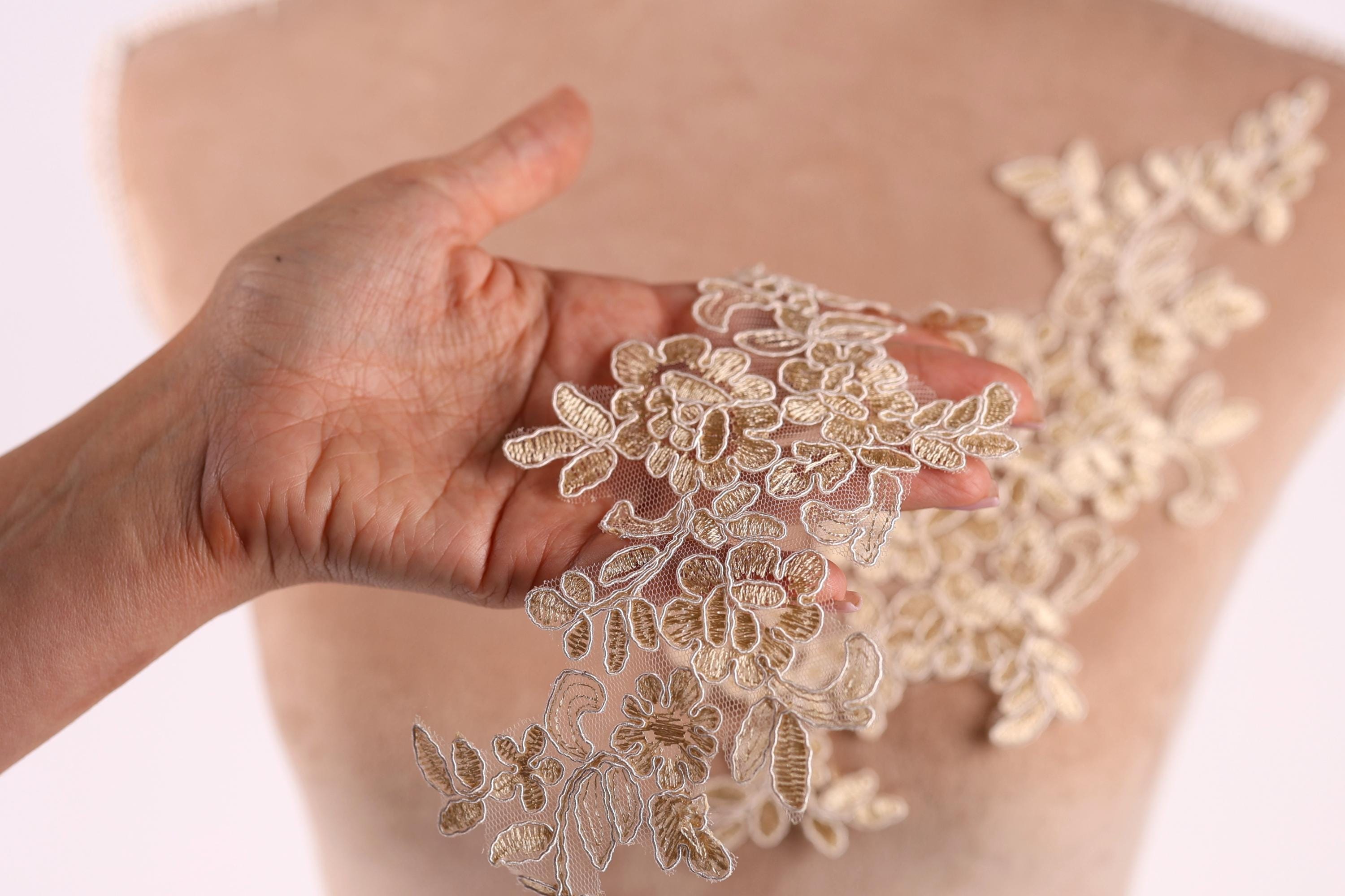 A hand holding a piece of fabric with intricate floral embroidery.