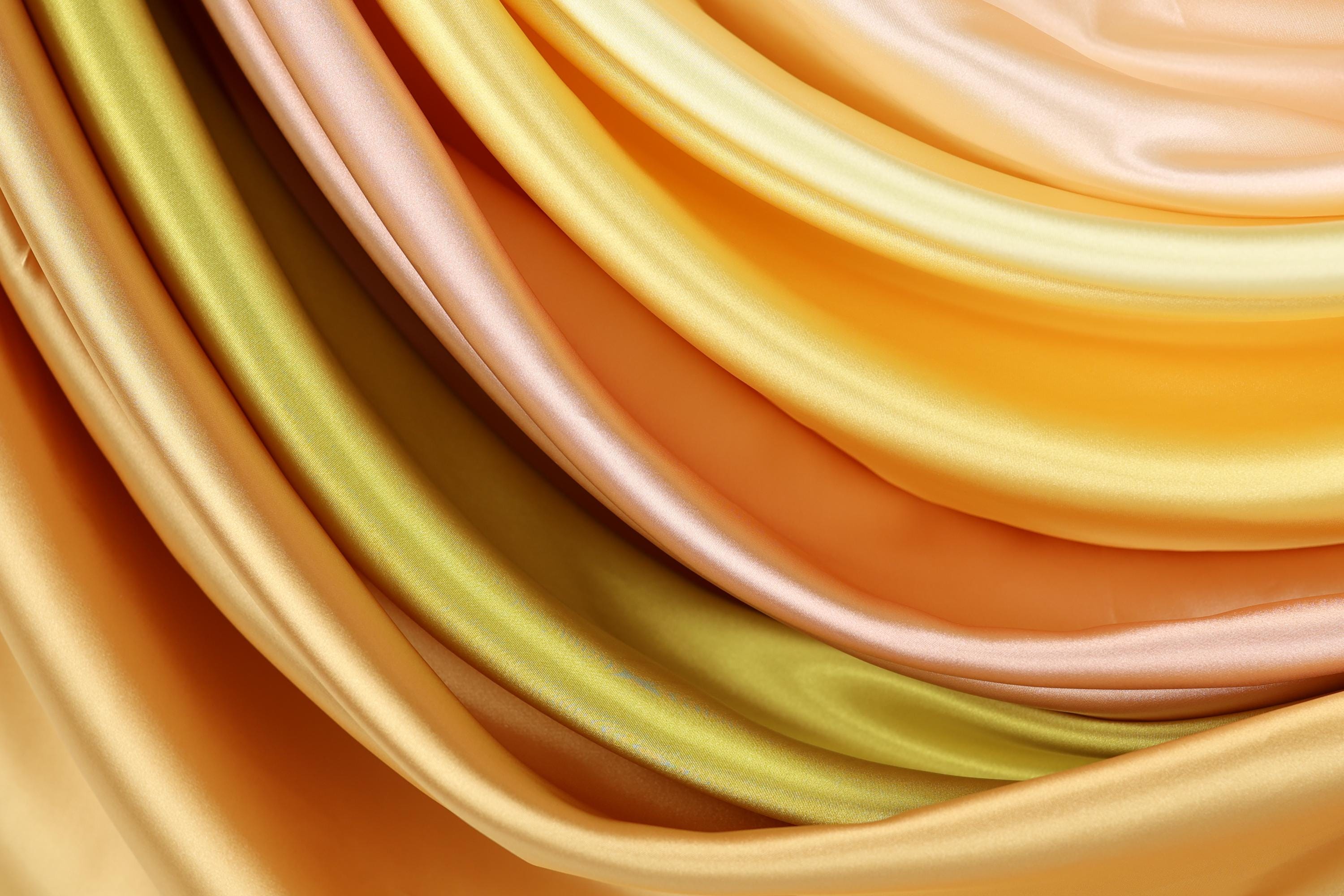 a close-up view of a variety of colorful satin fabric, including shades of yellow, orange, and green.