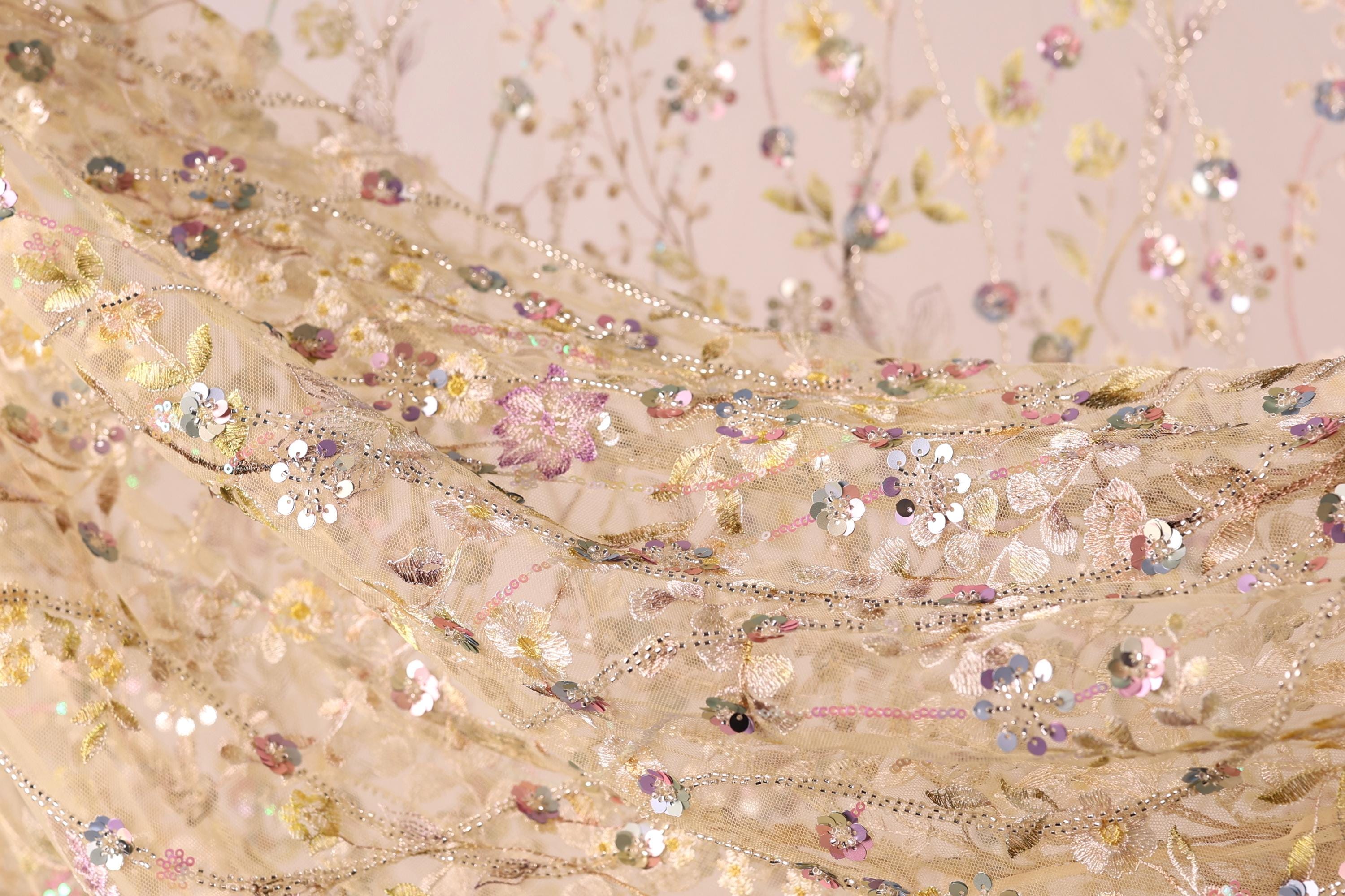 The image is a close-up of a delicate, intricately embroidered fabric with a floral pattern. The fabric is adorned with numerous small, colorful flowers and sequins, creating a visually striking and detailed design.