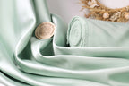 A close-up image of a light green satin fabric, with a small round metal object featuring text on it placed on the fabric.