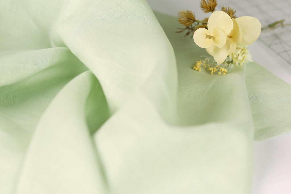 a close-up view of a light green fabric with a delicate yellow flower resting on top of it.