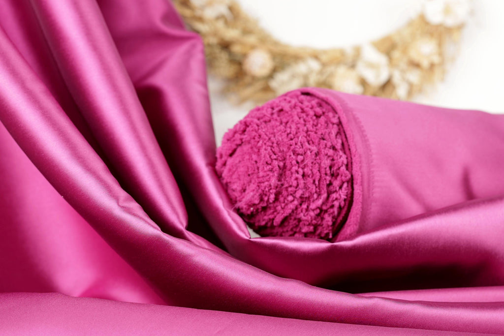A close-up view of a vibrant pink satin fabric, with a fluffy, textured object partially visible inside it.