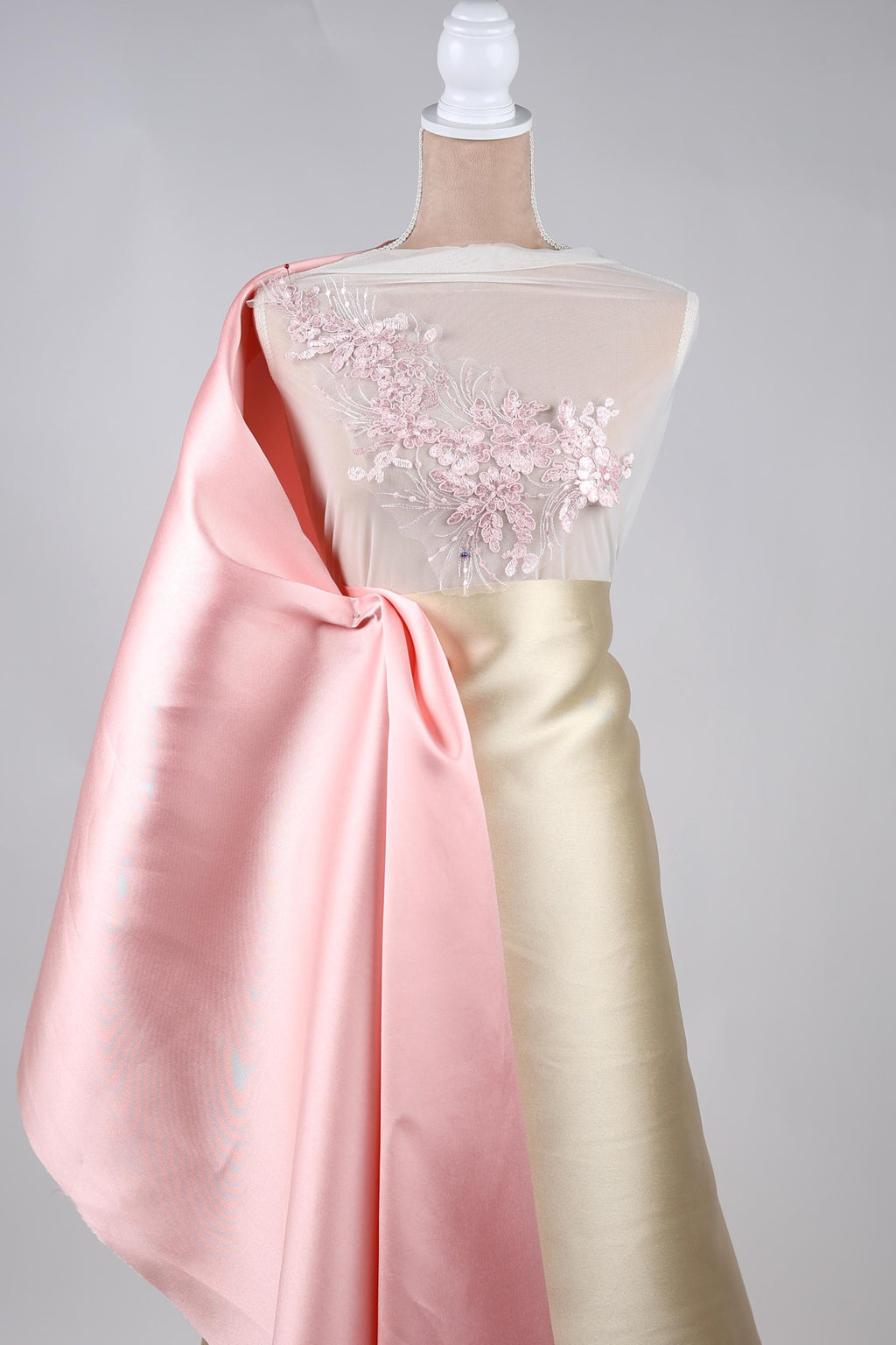 A mannequin wearing a pink satin cape and a gold satin skirt with a floral embellishment on the chest.