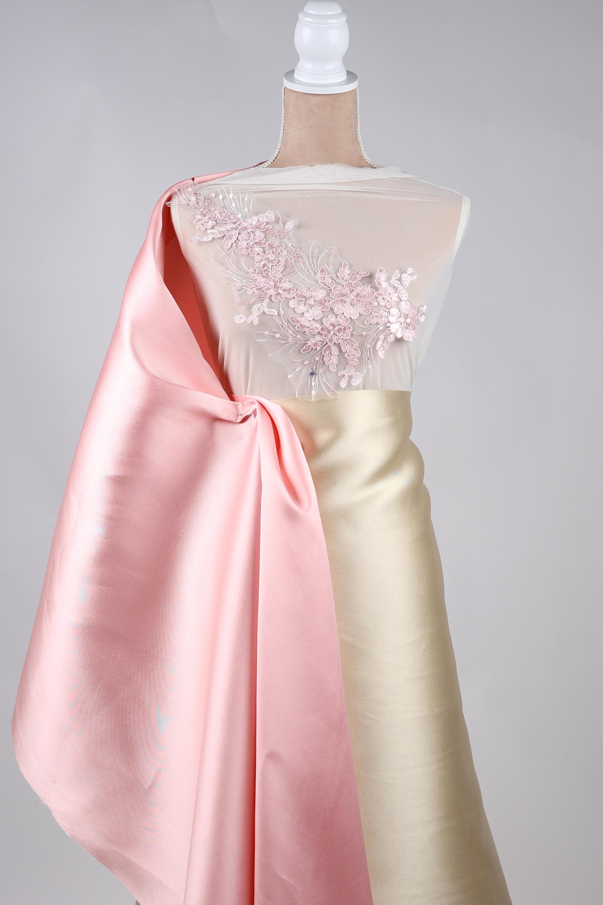 A mannequin wearing a pink satin cape and a gold satin skirt with a floral embellishment on the chest.