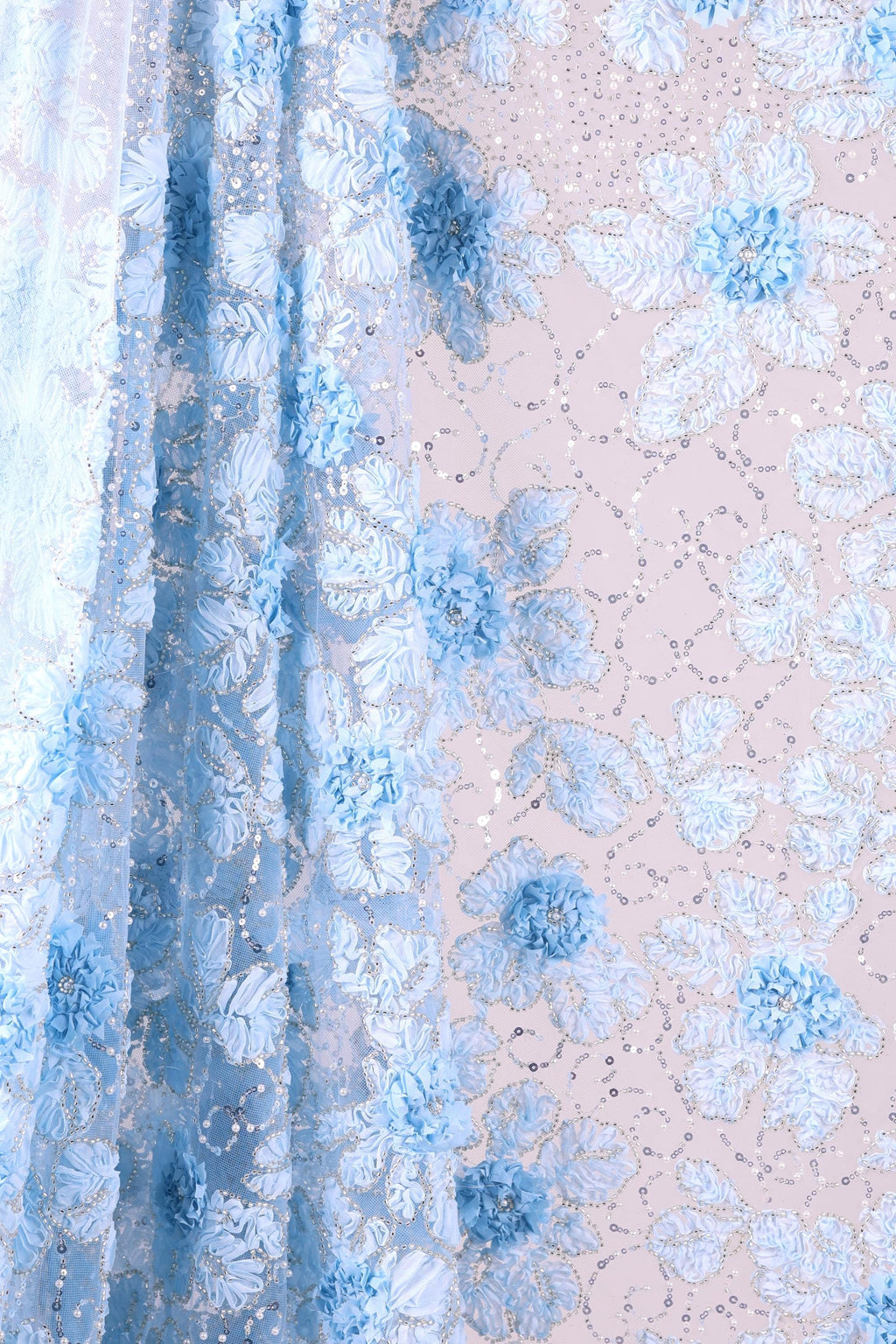 a close-up view of a fabric with a floral pattern in shades of blue and white. The fabric appears to be made of sheer material, with a delicate and intricate design. The pattern consists of various blue flowers and leaves, interspersed with small white dots or sequins, creating a visually appealing and textured appearance.