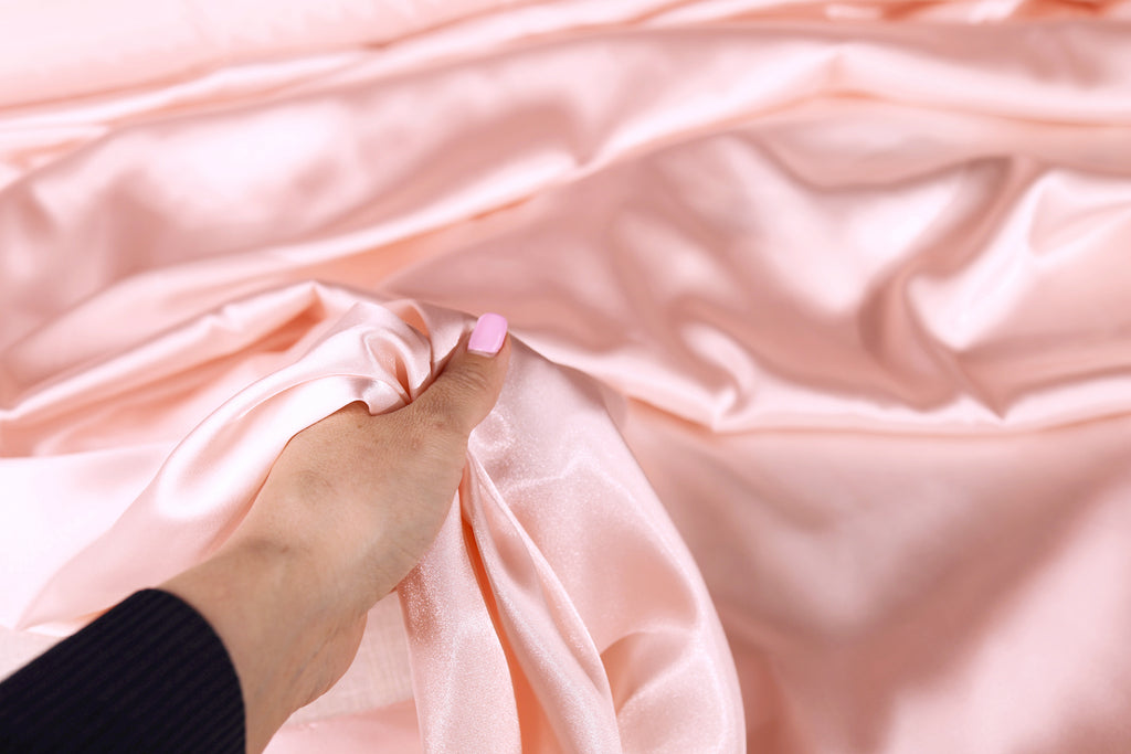 A hand holding a piece of pink satin fabric, with the fabric's folds and creases visible.