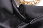 A close-up view of a black satin fabric, with a blurred floral arrangement in the background.