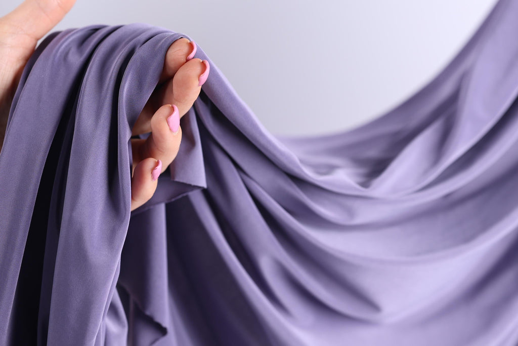 A hand holding a purple fabric, with the fabric partially draped over the hand.