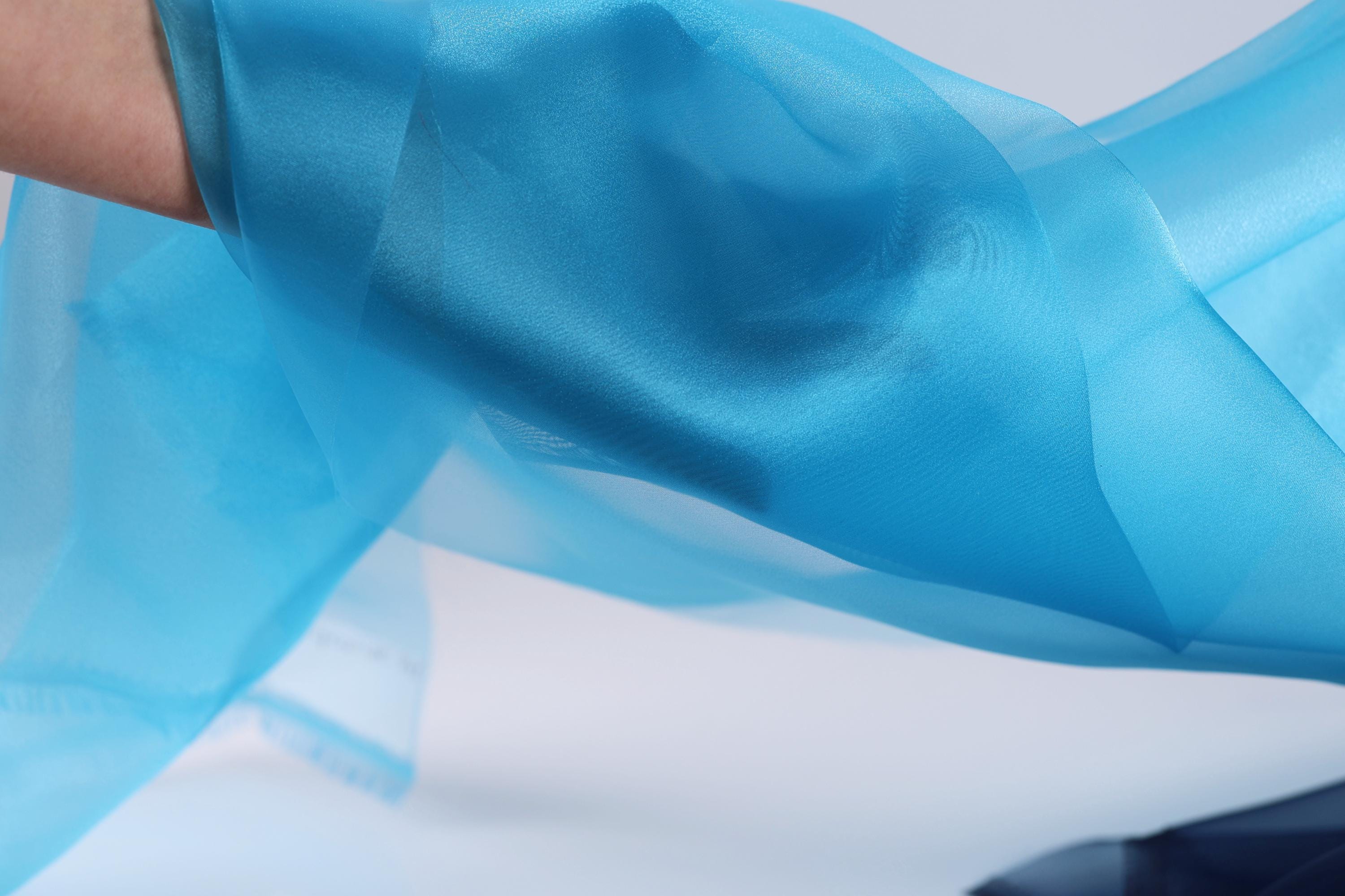 A close-up view of a blue fabric, possibly a scarf or garment, with a blurred background.