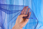 A hand is holding a piece of blue mesh fabric against a blue background.