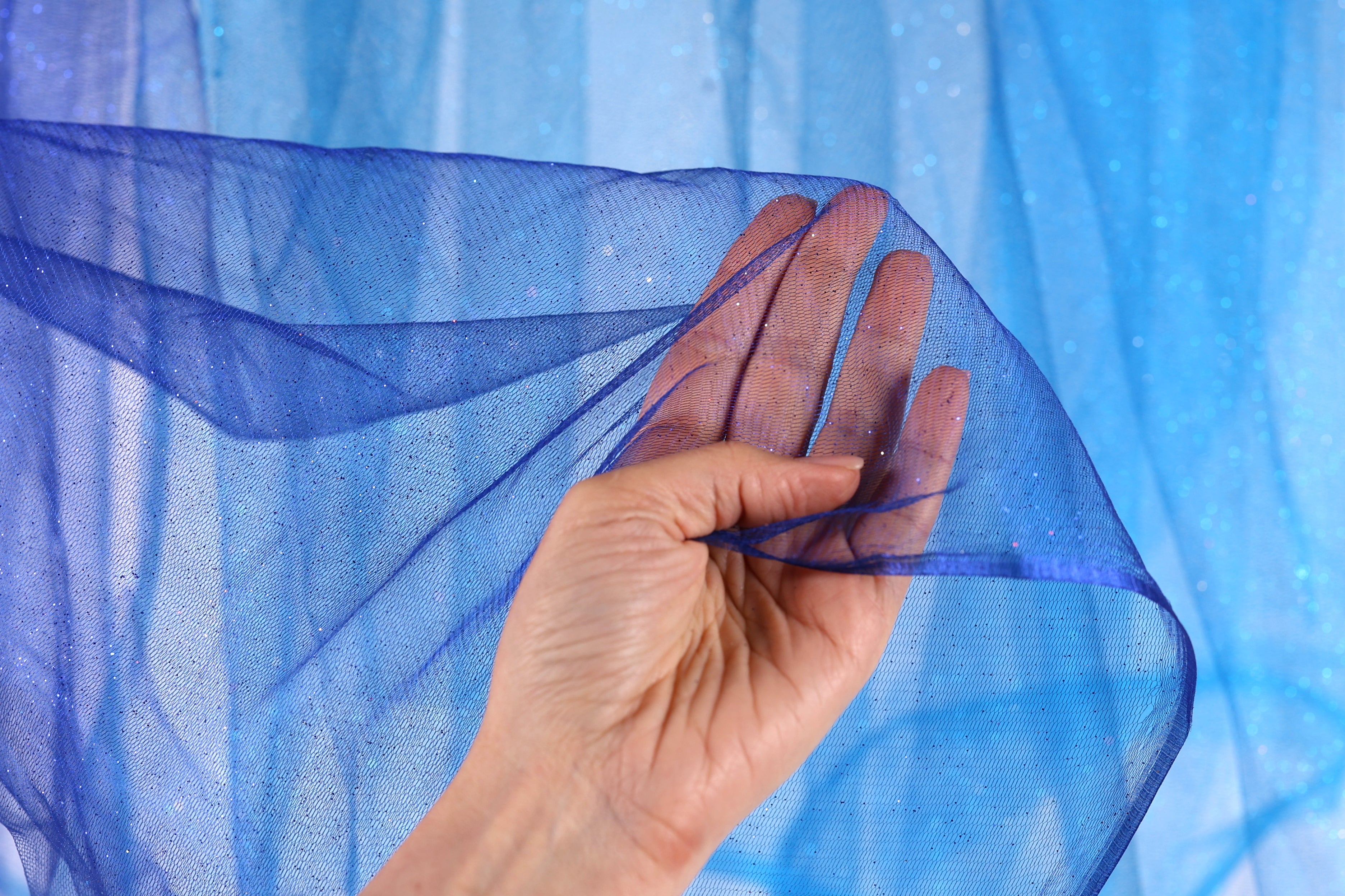 A hand is holding a piece of blue mesh fabric against a blue background.
