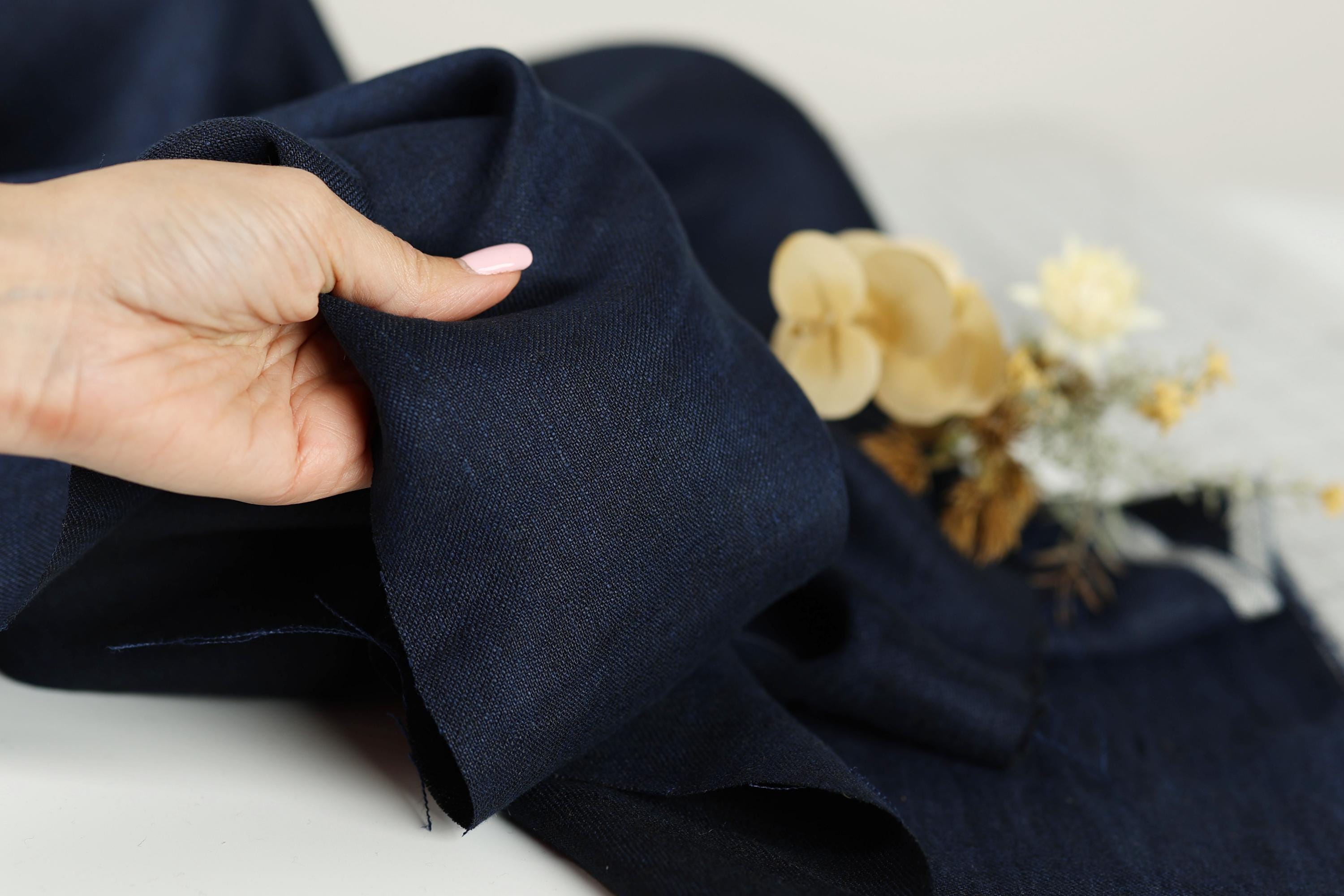 A hand is holding a piece of navy blue fabric, with a small bouquet of yellow flowers and dried flowers in the background.