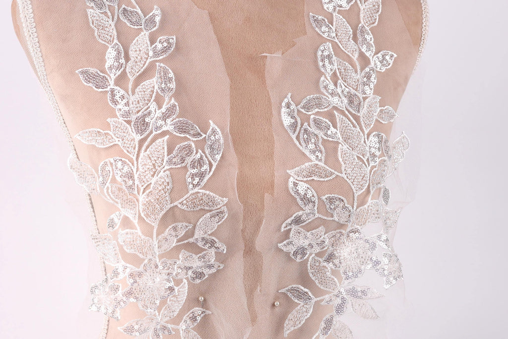 a close-up view of a delicate, lace-like fabric with intricate floral patterns. The fabric appears to be a sheer material, possibly a wedding dress or a bridal gown, with a lace bodice and a sheer overlay. The lace patterns are visible on the back of the fabric, creating a visually appealing and elegant design.