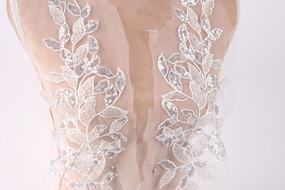 a close-up view of a delicate, lace-like fabric with intricate floral patterns. The fabric appears to be a sheer material, possibly a wedding dress or a bridal gown, with a lace bodice and a sheer overlay. The lace patterns are visible on the back of the fabric, creating a visually appealing and elegant design.