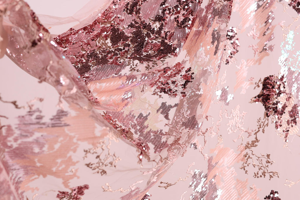 The image is a close-up of a fabric with a pink and red floral pattern, featuring sequins and lace-like textures.