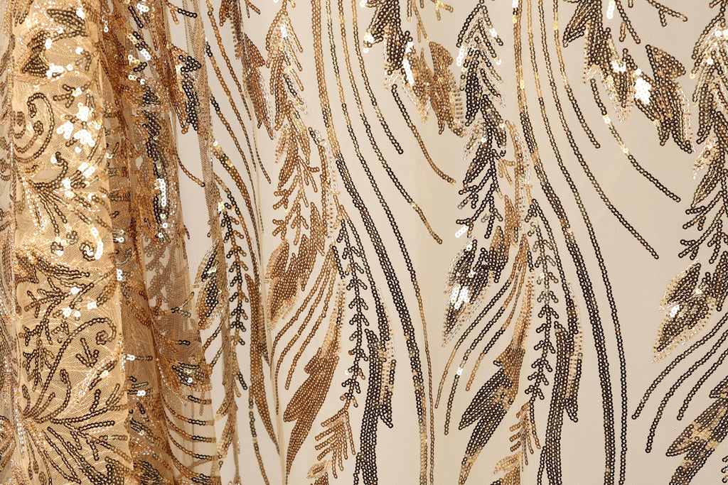 a close-up view of a fabric with a gold and black sequin pattern. The fabric appears to be a sheer material, with a repeating pattern of sequins and leaves. The pattern is intricate and detailed, with the sequins and leaves creating a visually striking design.