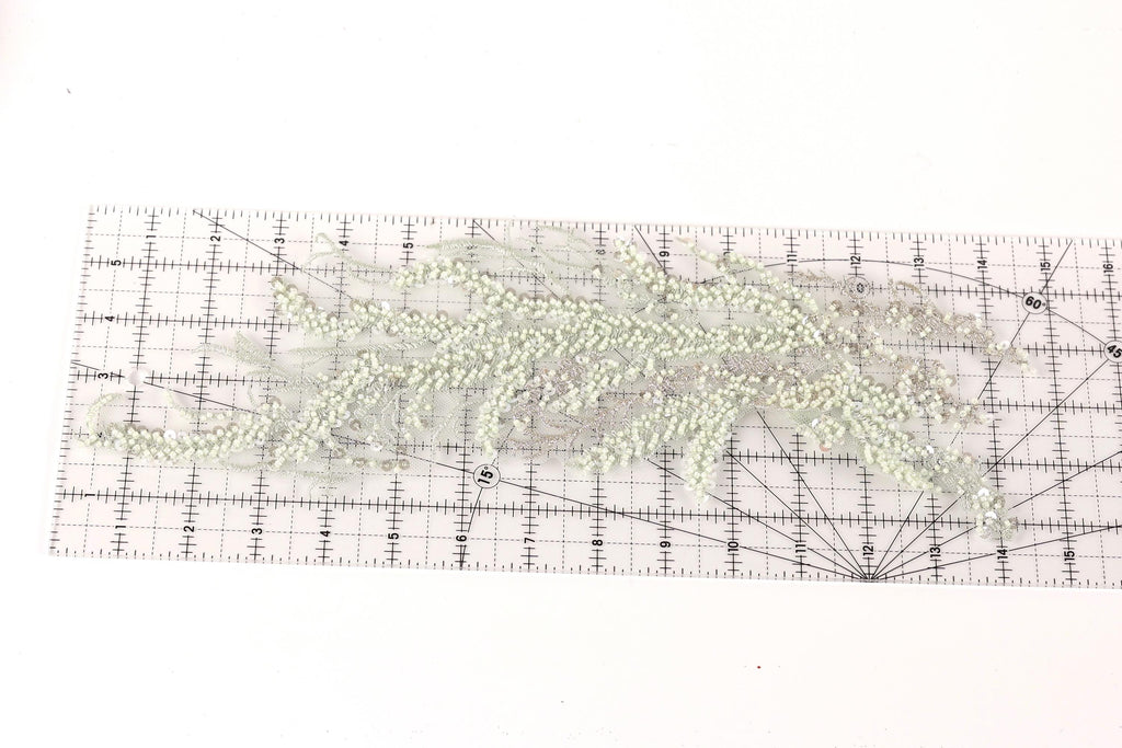 a transparent ruler with a grid pattern, placed on a white surface. The ruler is filled with small, white beads or sequins, creating a visually interesting and detailed pattern.