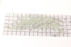 a transparent ruler with a grid pattern, placed on a white surface. The ruler is filled with small, white beads or sequins, creating a visually interesting and detailed pattern.