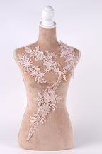 A mannequin with a beige body and a white headpiece, adorned with delicate pink floral lace pieces.
