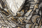 The image is a close-up of a fabric with a black and gold sequin pattern, featuring a mix of black, white, and gold sequins.