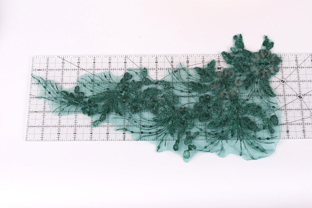 a piece of green lace with intricate floral patterns, laid out on a ruler for measurement purposes.