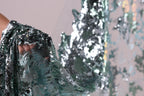 A close-up view of a sequin fabric, with a blurred background that appears to be a tree or plant.