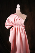 A pink satin one-shoulder dress displayed on a mannequin against a dark background.