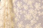 a close-up view of a fabric with a floral pattern, including white and yellow flowers and small silver sequins. The fabric appears to be a sheer material, with a delicate and intricate design.