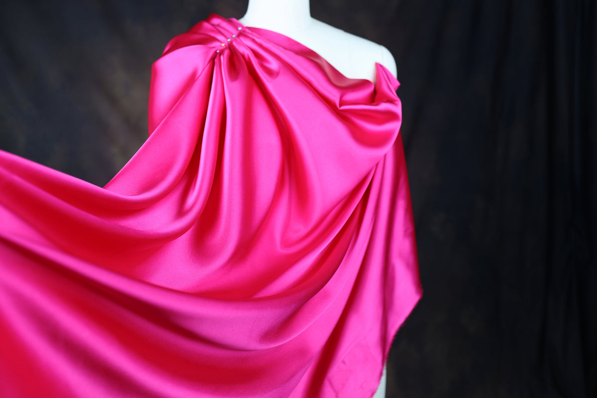 A mannequin wearing a vibrant pink satin dress with a flowing, draped design.