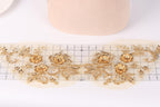 a close-up view of a delicate gold embroidered design on a white background. The design consists of intricate floral patterns and leaves, creating a visually appealing and elegant appearance.