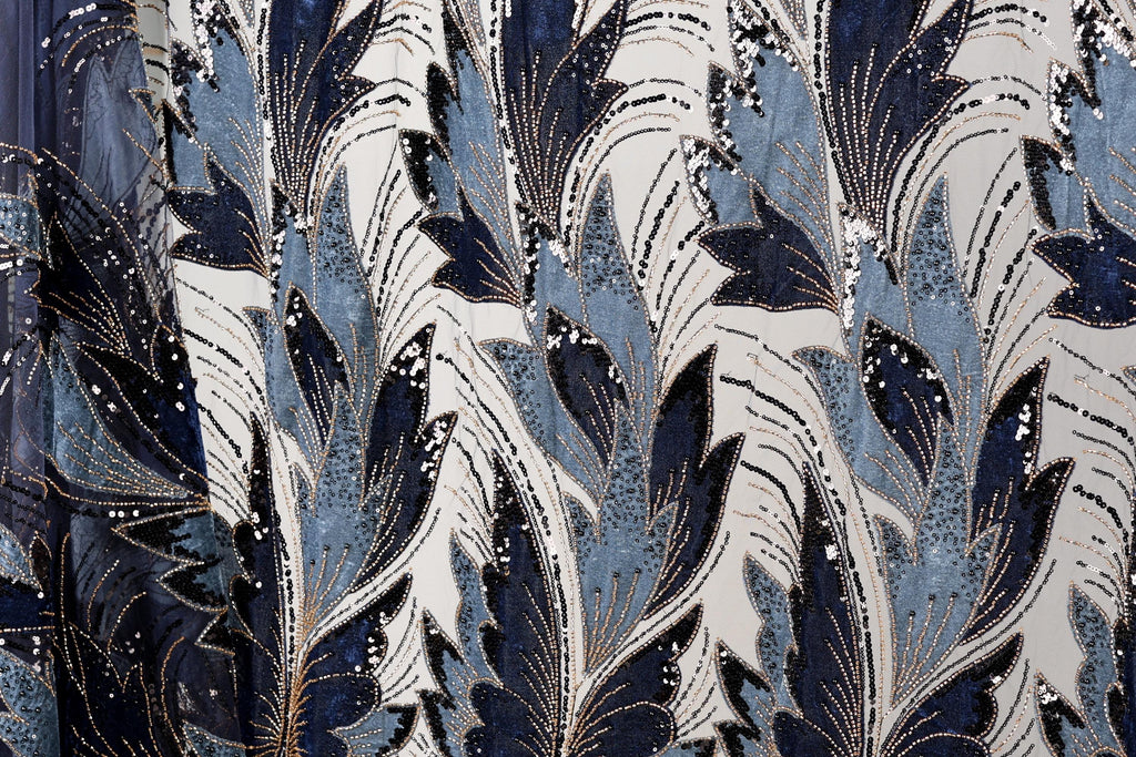 a close-up view of a fabric with a repeating pattern of blue and white leaves and flowers, adorned with gold sequins.