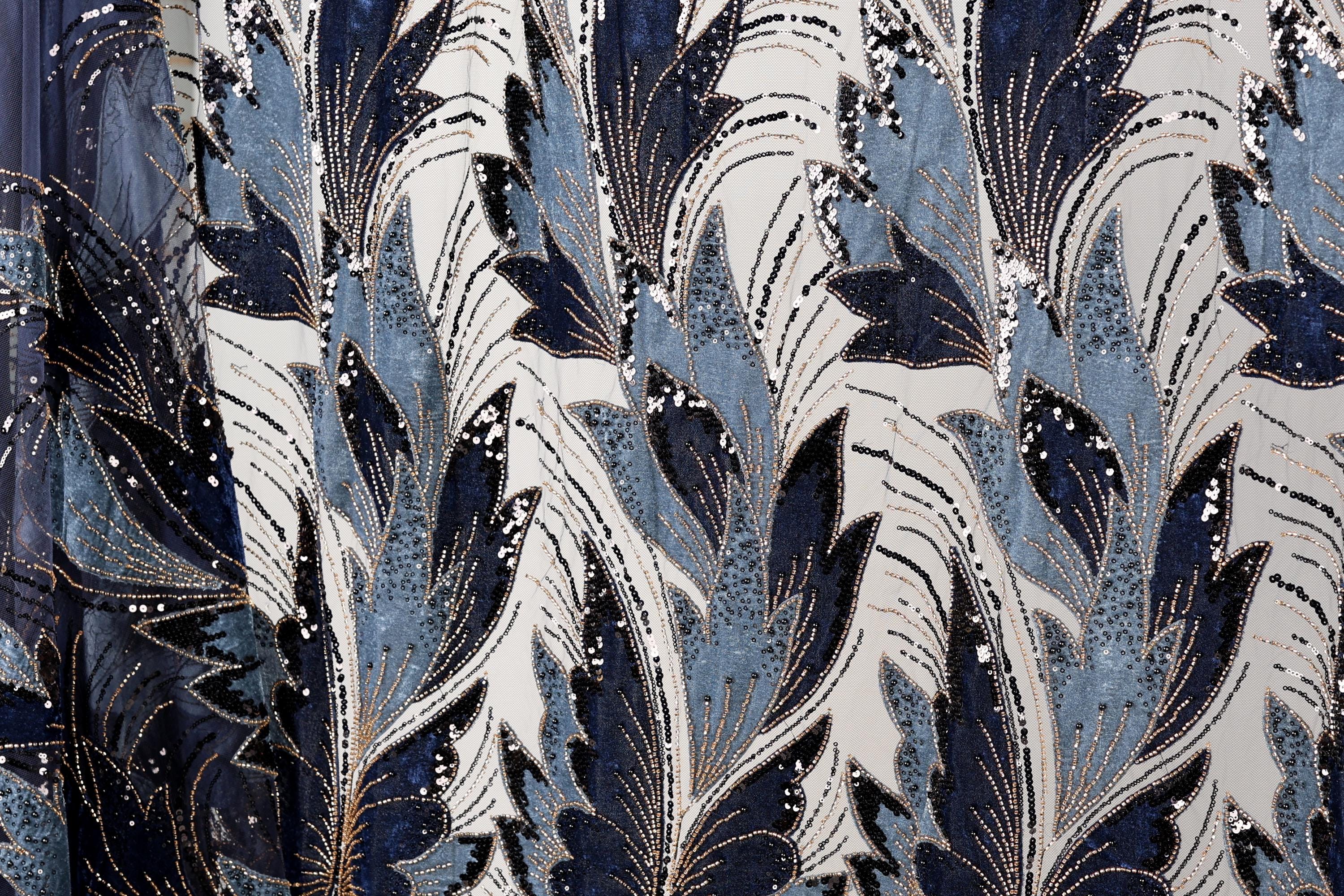 a close-up view of a fabric with a repeating pattern of blue and white leaves and flowers, adorned with gold sequins.