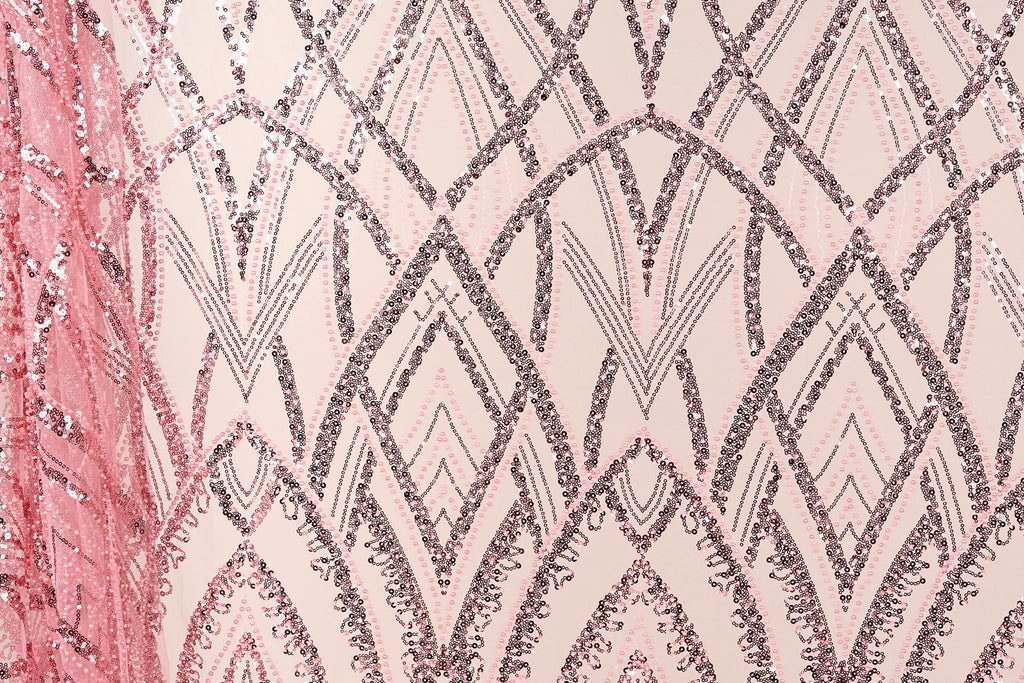 a close-up view of a fabric with a repeating pattern of pink and black sequin designs. The pattern consists of various diamond shapes and lines, creating a visually striking and intricate design. The fabric appears to be a piece of clothing or textile, with the pink and black colors contrasting against the neutral background.