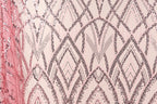 a close-up view of a fabric with a repeating pattern of pink and black sequin designs. The pattern consists of various diamond shapes and lines, creating a visually striking and intricate design. The fabric appears to be a piece of clothing or textile, with the pink and black colors contrasting against the neutral background.