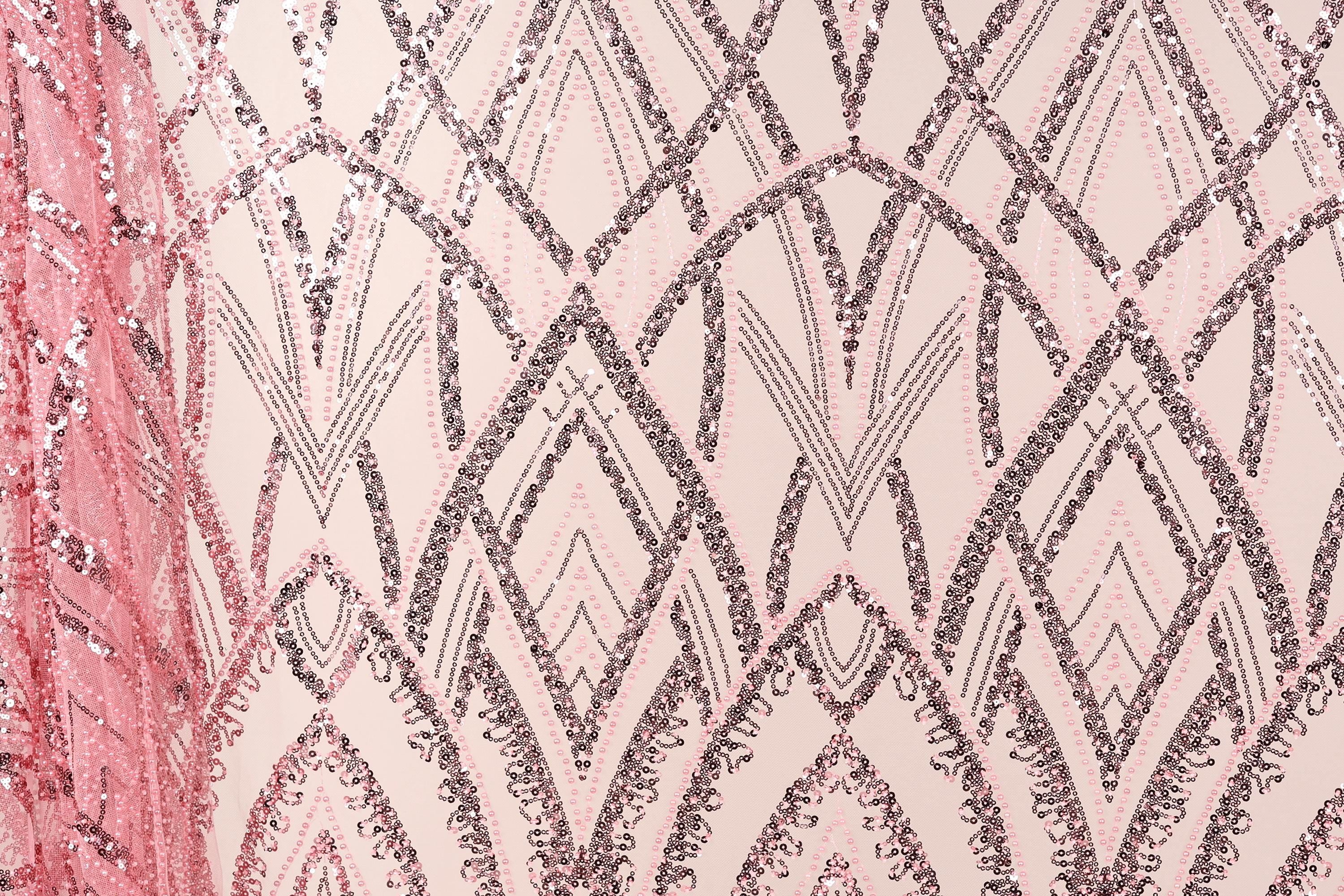 a close-up view of a fabric with a repeating pattern of pink and black sequin designs. The pattern consists of various diamond shapes and lines, creating a visually striking and intricate design. The fabric appears to be a piece of clothing or textile, with the pink and black colors contrasting against the neutral background.