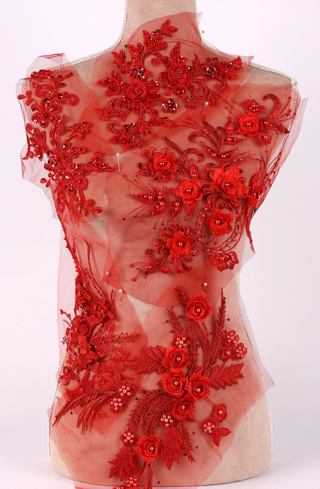 a mannequin with a red, sheer fabric dress adorned with intricate floral and leaf designs. The dress appears to be made of tulle and has a delicate, elegant appearance.