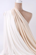 A mannequin wearing a white and beige draped fabric draped over its torso.