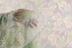 A hand is holding a piece of fabric with a green and silver pattern, against a blurred background.