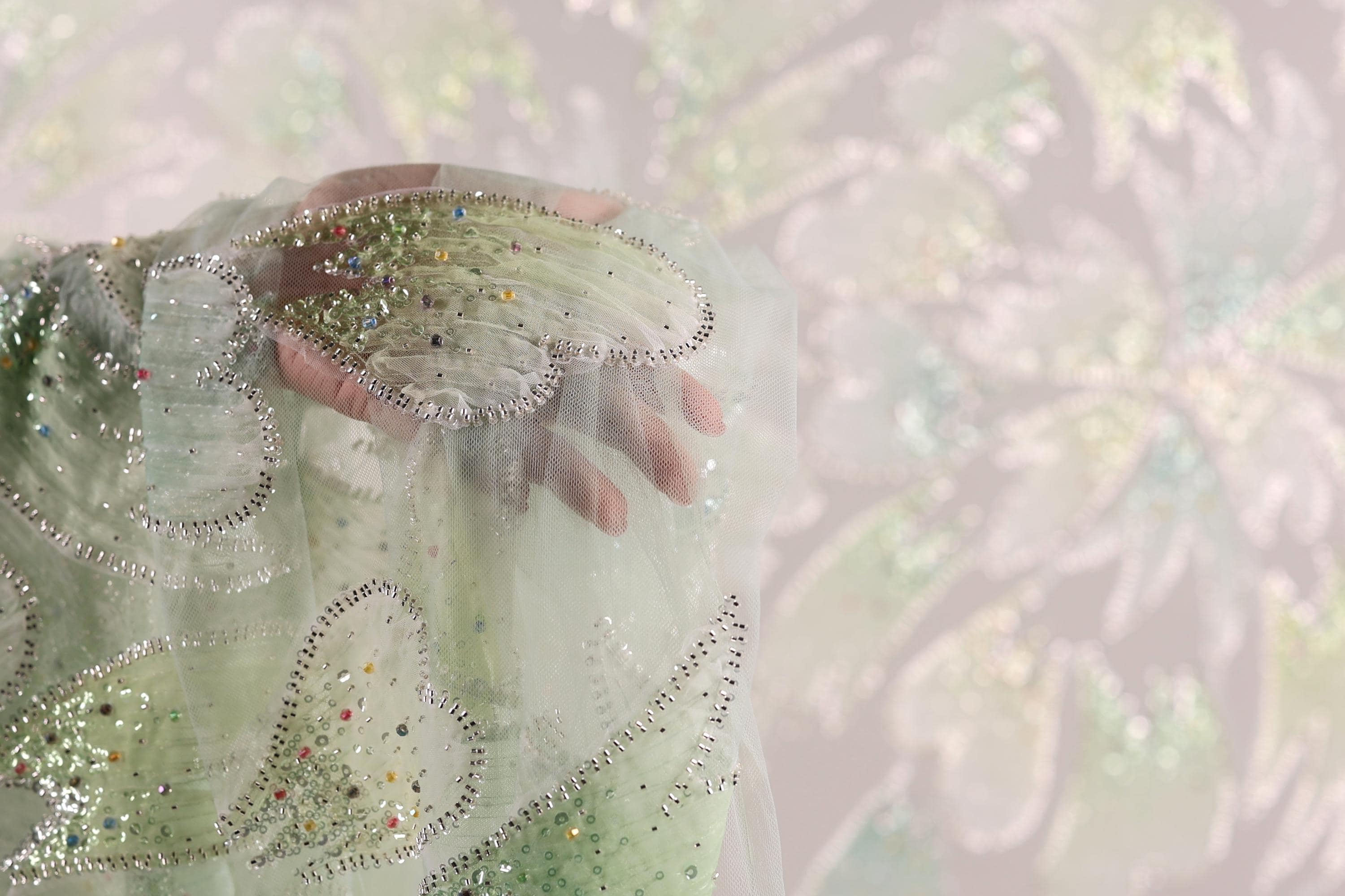 A hand is holding a piece of fabric with a green and silver pattern, against a blurred background.