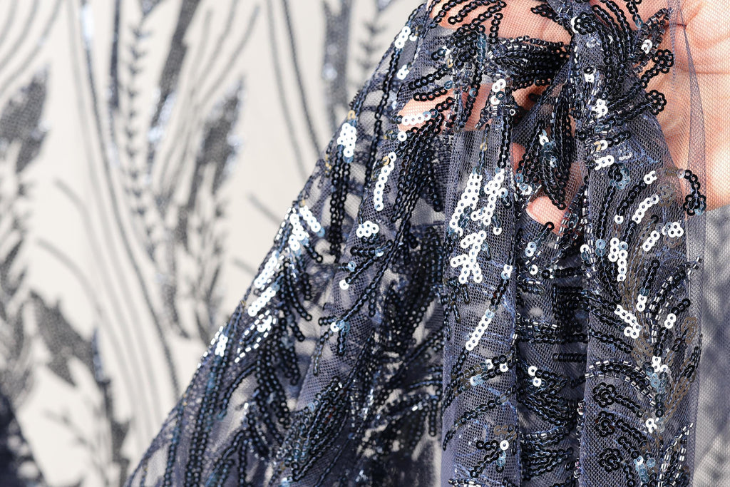A close-up view of a hand holding a piece of fabric with a black and white floral pattern, featuring sequins and beads.