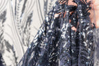 A close-up view of a hand holding a piece of fabric with a black and white floral pattern, featuring sequins and beads.