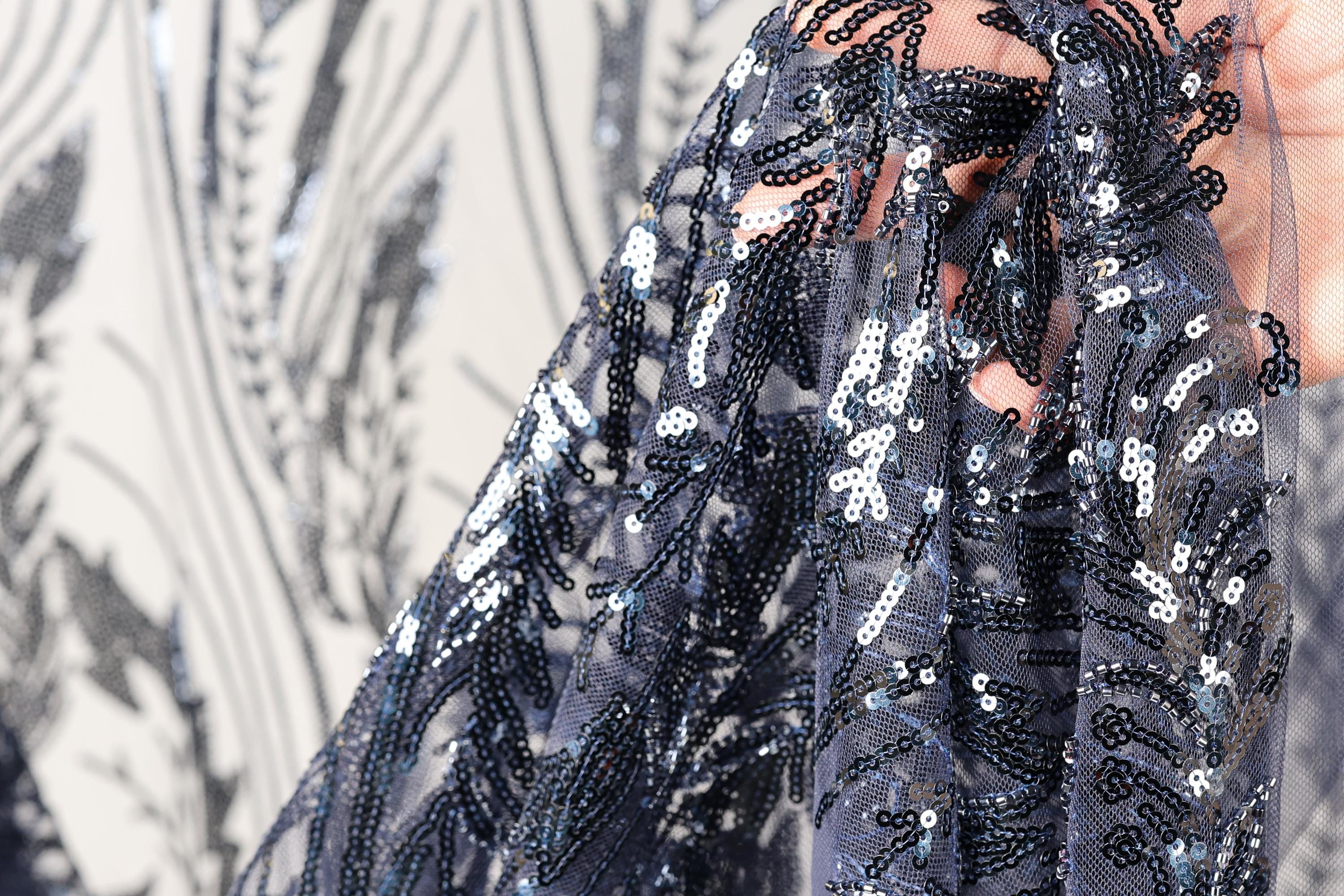 A close-up view of a hand holding a piece of fabric with a black and white floral pattern, featuring sequins and beads.