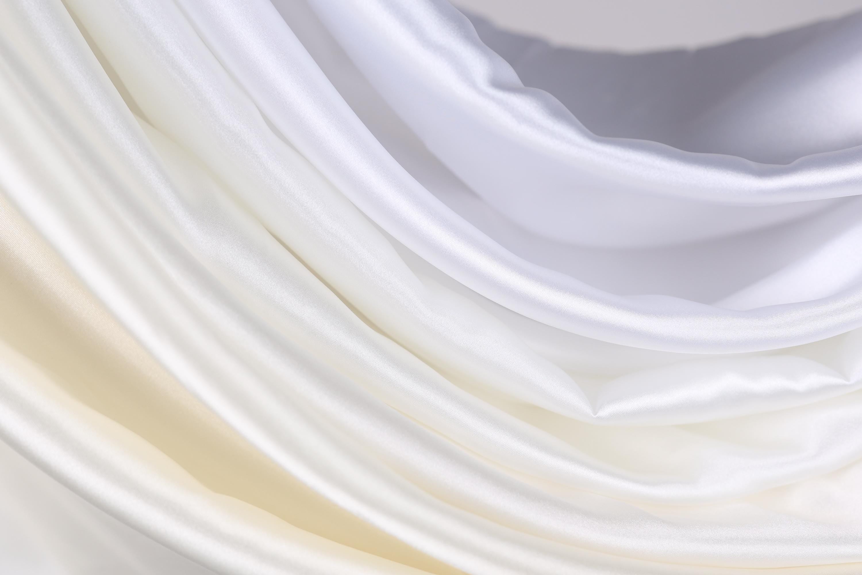 The image is a close-up of a soft, flowing fabric with a gradient of white and yellow colors. The fabric appears to be made of silk or satin, and it has a smooth, shiny texture. The colors are vibrant and the fabric is draped in a way that creates a sense of movement and softness.