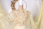 A mannequin wearing a yellow lace dress with a floral pattern, displayed against a white background with a wreath.