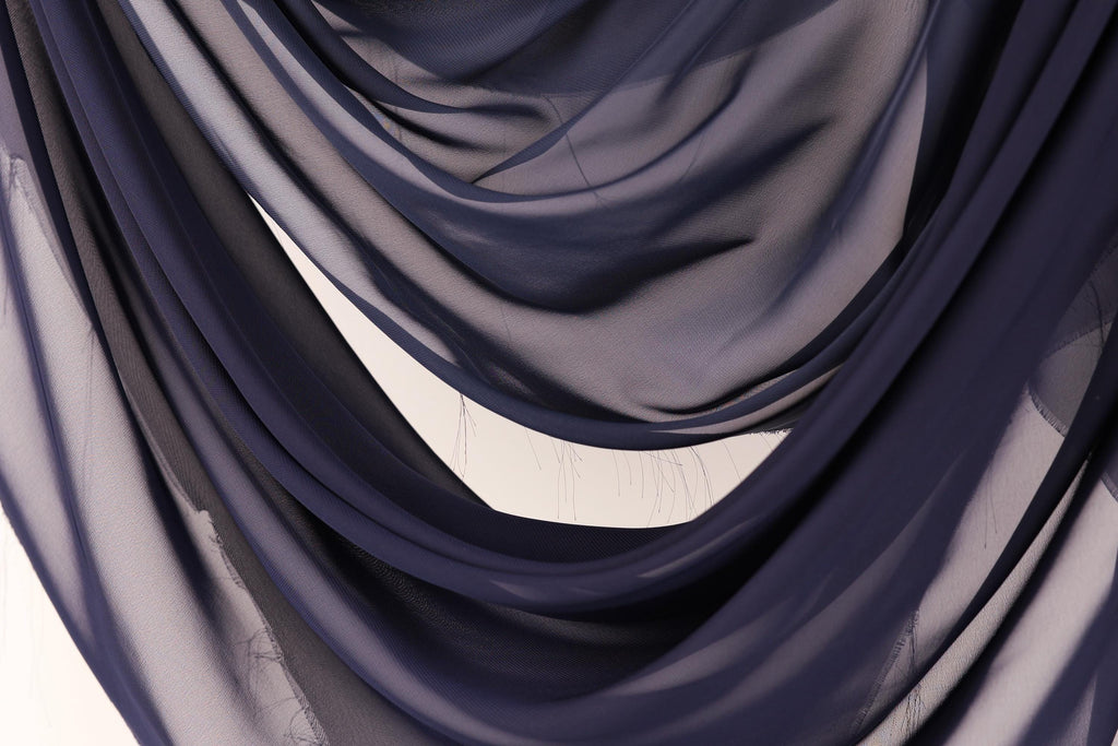 a close-up view of a fabric with a dark blue color, possibly a chiffon or a similar type of material. The fabric appears to be folded or draped in a way that creates a sense of depth and texture.
