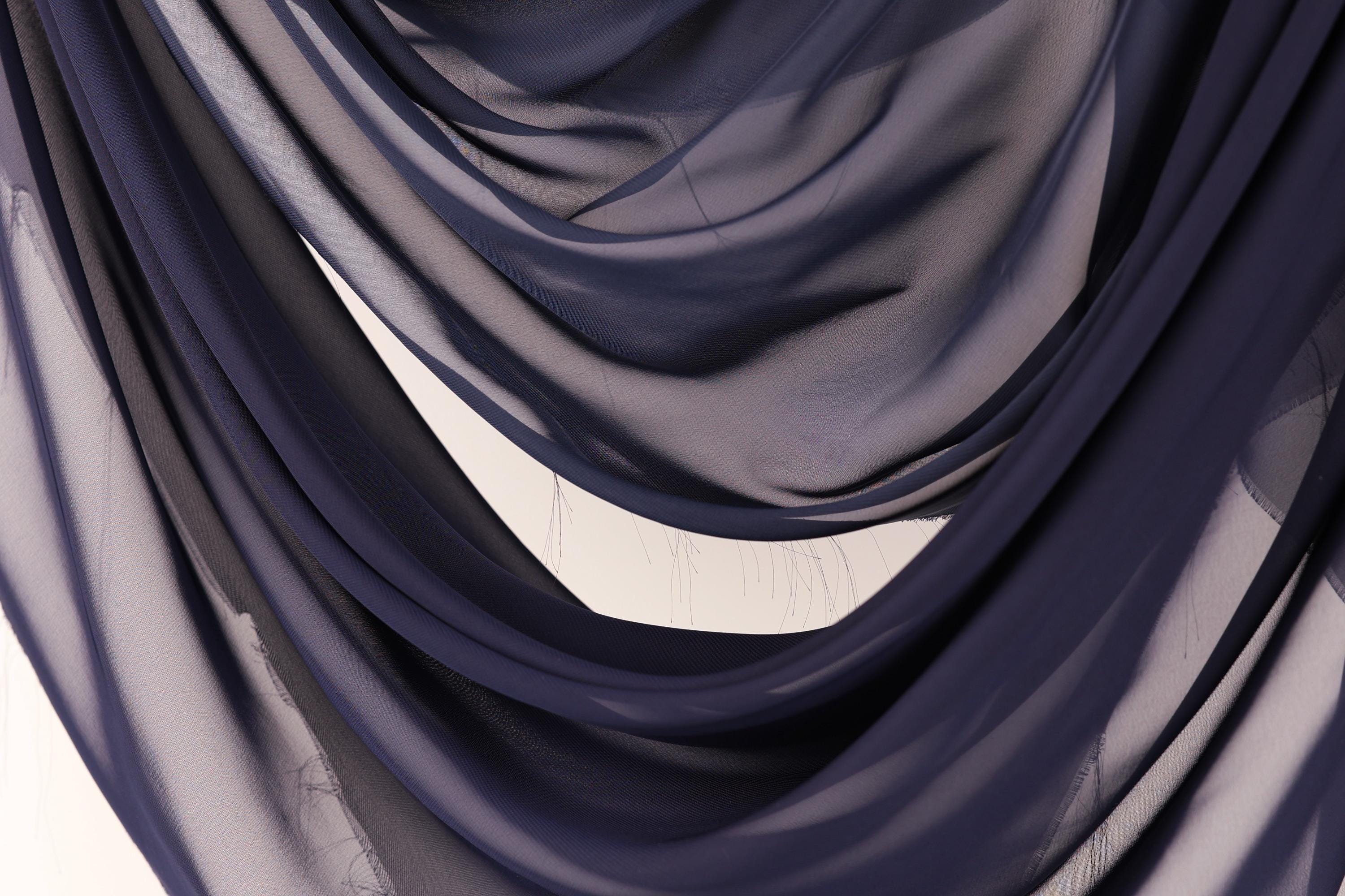 a close-up view of a fabric with a dark blue color, possibly a chiffon or a similar type of material. The fabric appears to be folded or draped in a way that creates a sense of depth and texture.